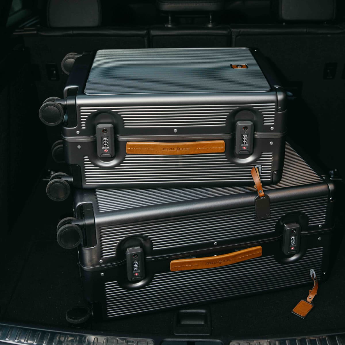 Two silver Carry-On suitcases with tan leather handles stacked in a car boot