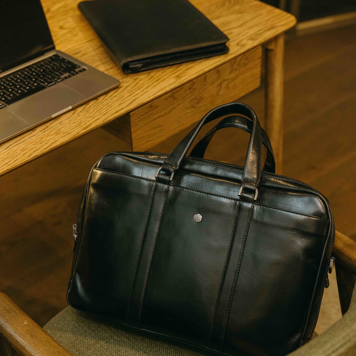 Black leather Laptop Briefcase on a chair beside a desk with a laptop and wallet