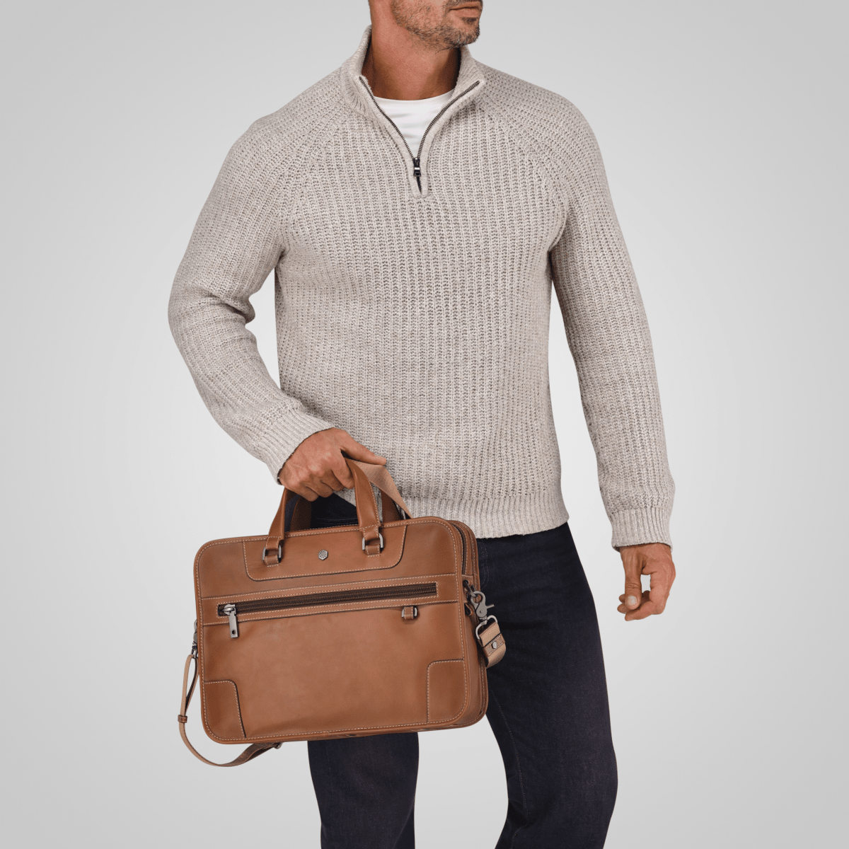 Man in a cream knit jumper carrying the Colt tan leather Medium Briefcase by its handles