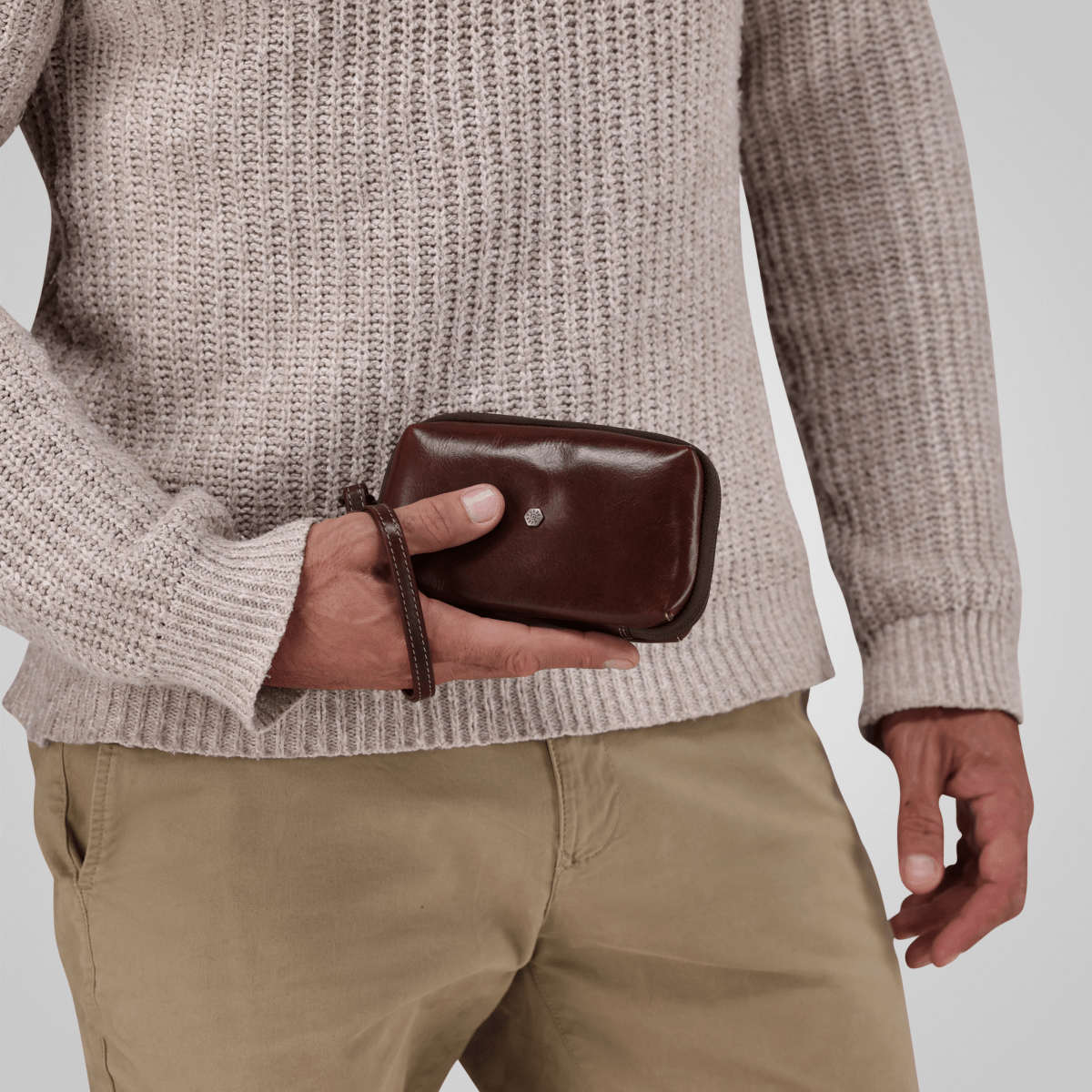Man holding the Mocha leather Cable Pouch in one hand, wrist strap looped