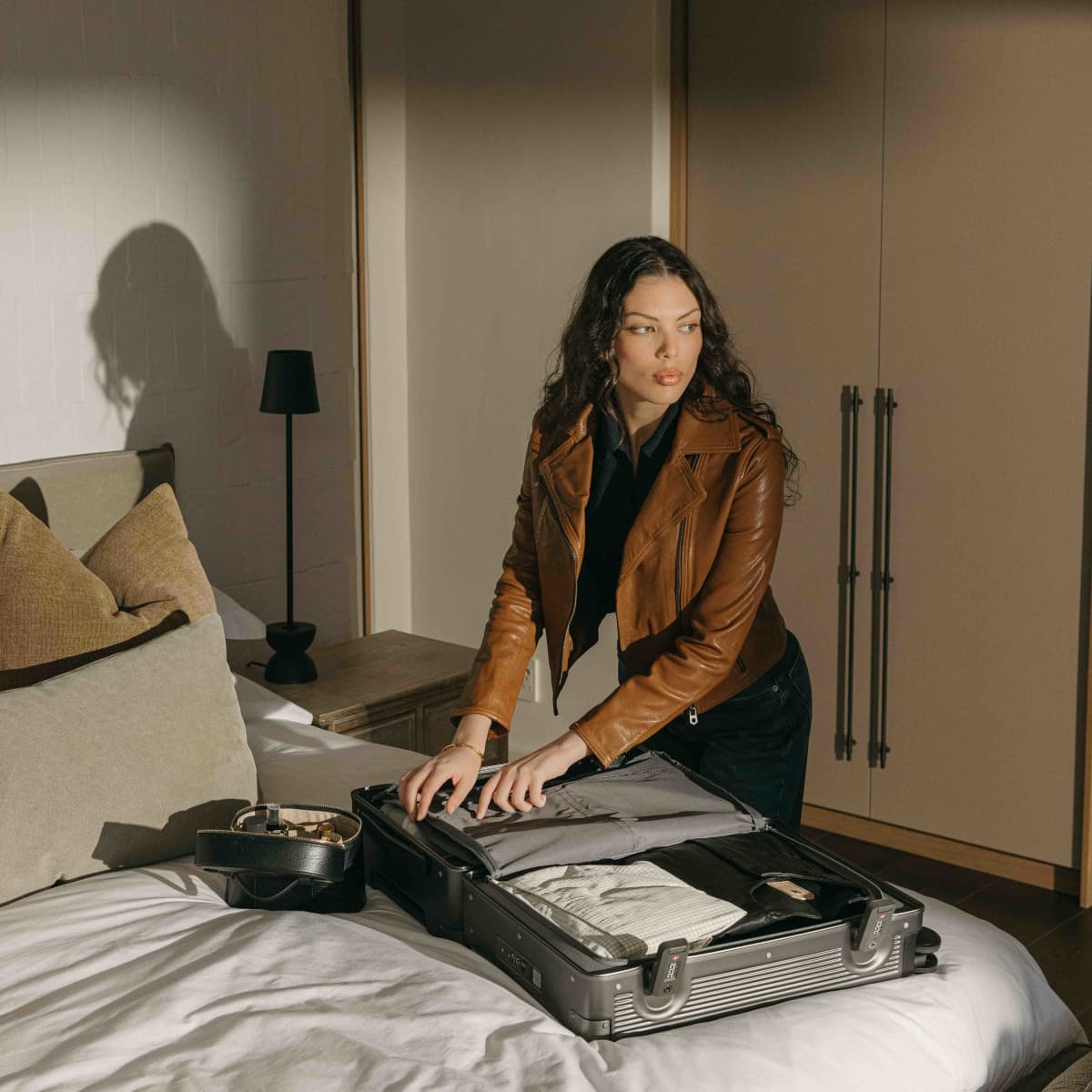 Woman packing the open silver Carry-On suitcase on a hotel bed