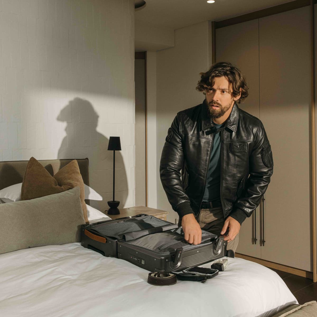 Man packing the open silver Carry-On suitcase on a hotel bed