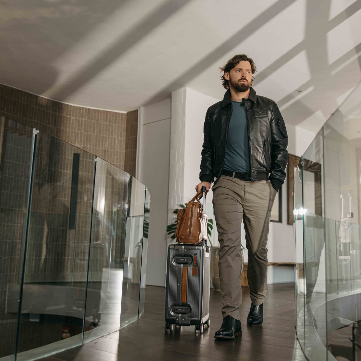 Man walking through a hotel atrium wheeling the silver Carry-On suitcase