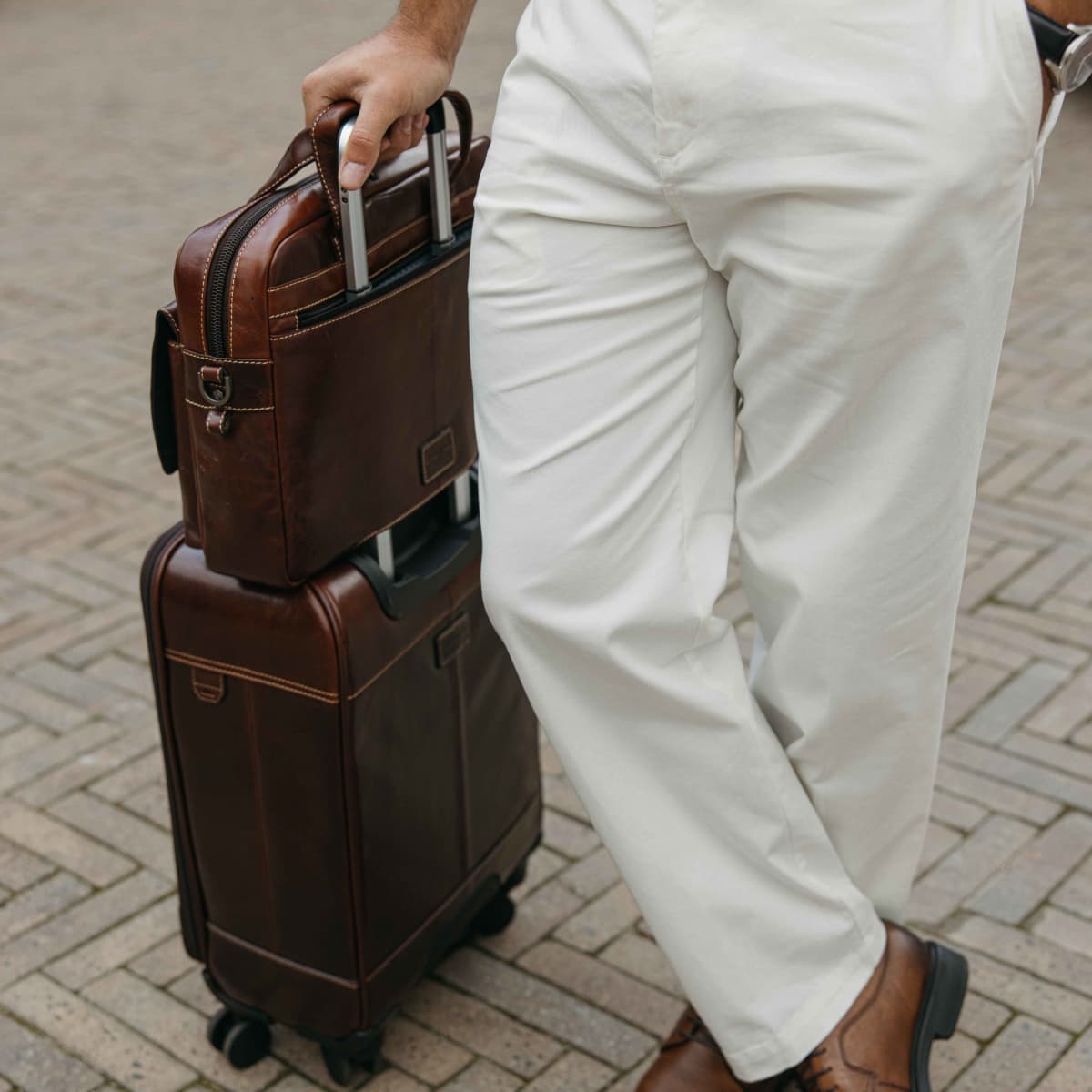 Mocha leather Laptop Briefcase sitting on a wheeled suitcase on a brick driveway