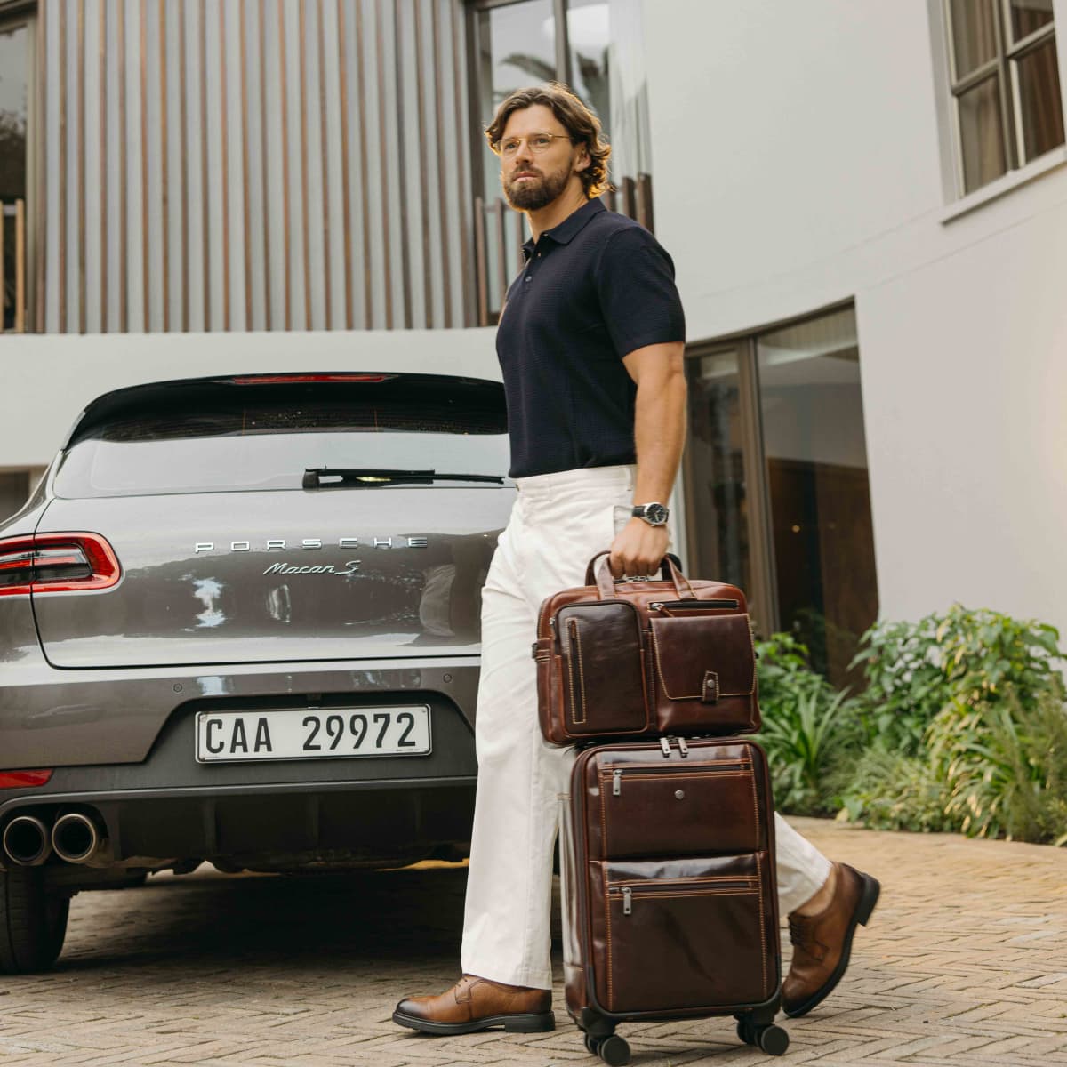 Man wheeling a suitcase with the Mocha leather Laptop Briefcase on top, beside a car