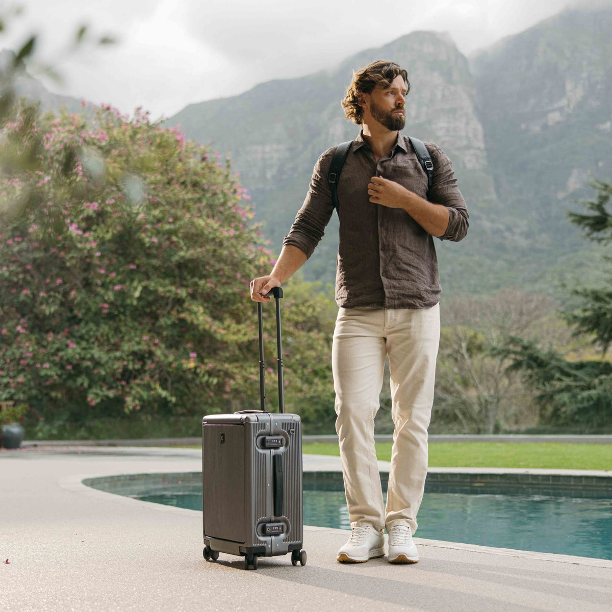 Man with the Jekyll & Hide graphite-black Carry-On suitcase beside a pool with mountains behind