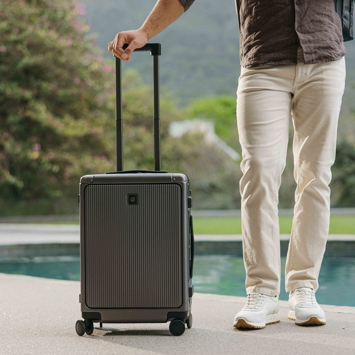 Jekyll & Hide graphite-black Carry-On with trolley handle extended, standing beside a man by a swimming pool