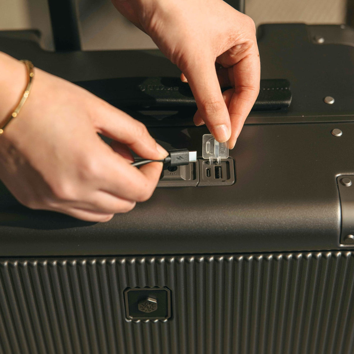 Hand plugging a cable into the built-in USB charging port on the Jekyll & Hide graphite-black Carry-On